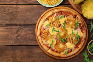 Delicious pineapple pizza and ingredients on wooden table, flat lay. Space for text