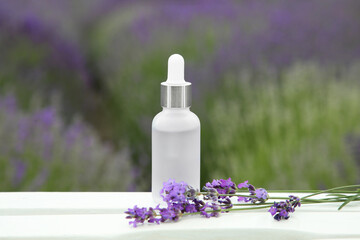 Obraz na płótnie Canvas Bottle of essential oil and lavender flowers on white wooden table in field