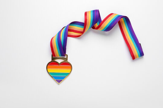 Rainbow ribbon with heart pendant on white background, top view. LGBT pride