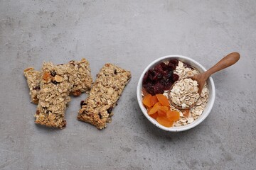 Tasty granola bars and ingredients on grey table, flat lay