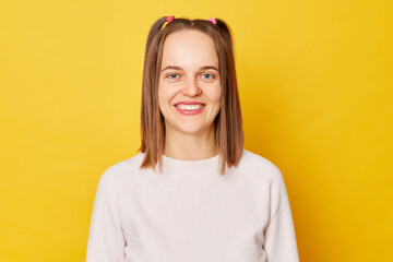Smiling attractive charming teenage girl in jumper with ponytails isolated over yellow background...