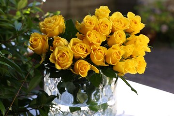 Beautiful bouquet of yellow roses in glass vase on white table outdoors
