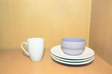 White dishes: a mug, plates, a coarse white bowl on a shelf in the cupboard