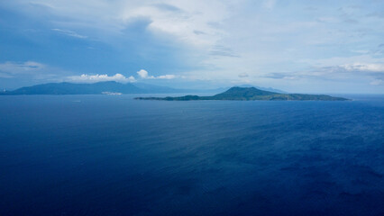 Uninhabited island in the Pacific Ocean and white clouds. Aerial view of a small uninhabited tropical island in a strait among the islands.