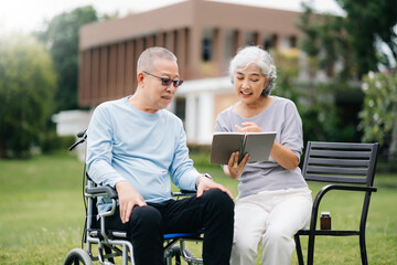 Asian Senior couple sitting in wheelchairs taking care of each other.in romantic time They laughing and smiling while sitting outdoor in park..