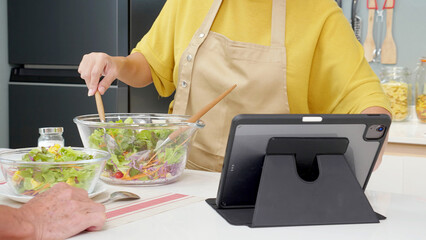 Closeup hands asian senior couple watching recipe with tablet making salad vegetable together in...