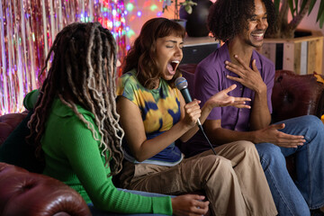 Young adult friends singing karaoke together and laughing