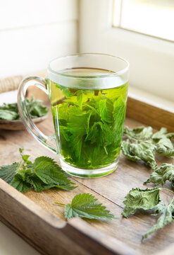 Herbal tea made of dry Urtica dioica, known as common nettle, burn nettle or stinging nettle leaves in clear glass cup. In home kitchen by the window.