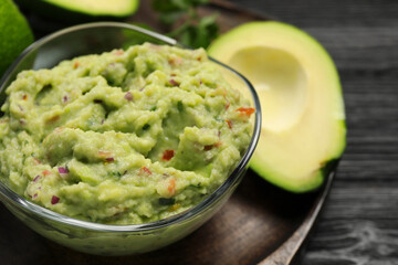 Glass bowl with delicious guacamole and fresh avocado on table, closeup. Space for text