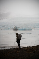 Mężczyzna spogląda na lodowiec, któ®y jest widoczny w jego tle, Islandia - obrazy, fototapety, plakaty