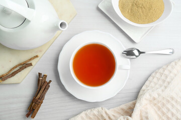 Fototapeta na wymiar Aromatic licorice tea in cup served on white wooden table, flat lay