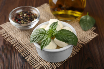 Tasty mozarella balls and basil leaves in bowl on wooden table, closeup
