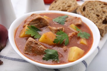 Delicious goulash in bowl on white table, closeup