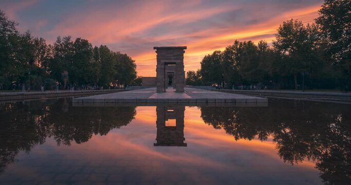 Front symmetrical view timelapse of Templo de Debod temple during colorful and beautiful clouds and sunset in Madrid with perfect reflection park
