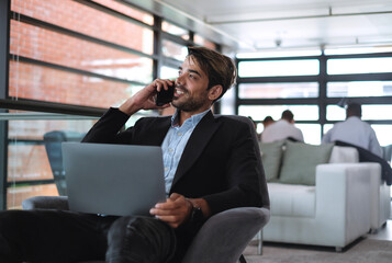 Handsome caucasian businessman talking on the phone while working with laptop in the modern office.