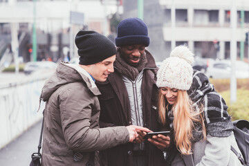 Fototapeta premium three young friends together in modern city and looking smartphone