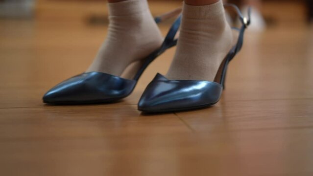 Closeup tracking shot of little female feet putting on high-heels walking on parquet floor indoors. Close-up unrecognizable cheerful Caucasian girl having fun at home