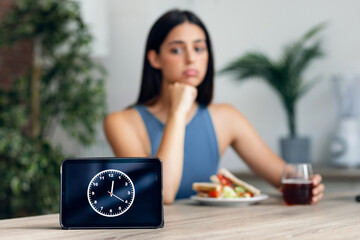 Hungry sporty woman waiting for the time to eat after fasting in the kitchen at home
