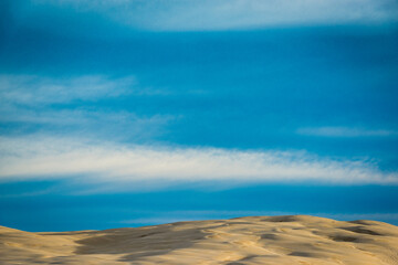 Sand dunes shot at sunrise in front of a blue sky with white clouds in the sky. There is a sense of isolation in the photo. 