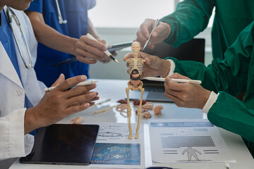 A multi-ethnic medical team is meeting with doctors in white lab coats and surgical gowns who sit at tables to discuss patient records, find a cure. Image of a group of doctors talking together