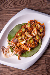 grilled bbq fresh whole seafood squid sooting octopus with spicy samba chilli sauce and petai smelly bean vegetables in banana leaf plate on wood table asian restaurant banquet cuisine halal food menu
