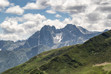 Fototapeta premium Mountain landscape with green slopes, cliffs, glaciers and white clouds in the sky
