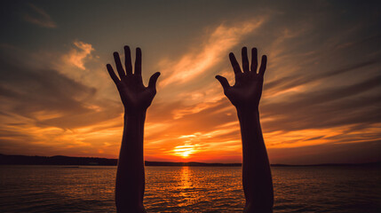 Two raised hands on the beach during sunset.