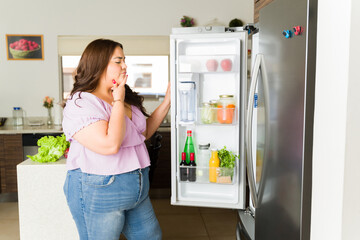 Fototapeta na wymiar Pensive woman opening the fridge opening the fridge in the kitchen