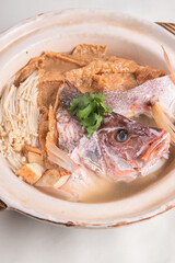 local boiled cook live fresh red grouper fish head seafood bean curd skin mushroom with hot herbal pepper soup in big casserole clay pot on wood table asian restaurant banquet cuisine halal food menu