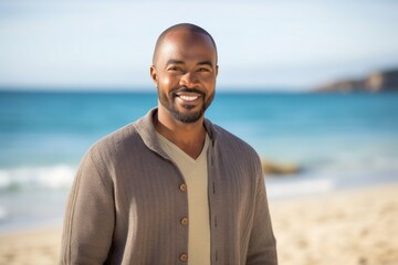 portrait of a confident Kenyan man in his 40s wearing a chic cardigan against a beach background