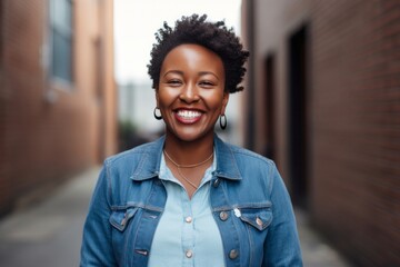 Portrait of a happy Kenyan woman in her 30s wearing a denim jacket against a minimalist or empty room background - obrazy, fototapety, plakaty