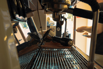 Close-up shot of a small cafe's espresso machine in the early morning from behind the bar hile a barista, a skilled artisan, works in the background. The coffee machine stands as the focal point