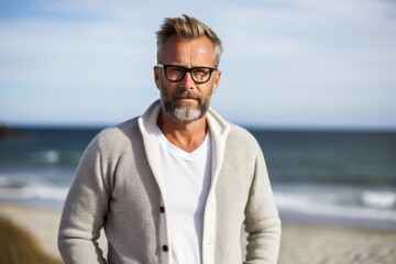 portrait of a confident Polish man in his 40s wearing a chic cardigan against a beach background