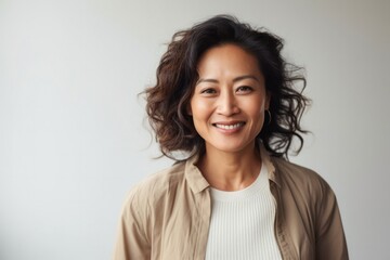 Portrait of a Filipino woman in her 50s wearing a chic cardigan against a minimalist or empty room background
