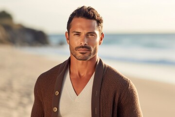 portrait of a serious, Mexican man in his 30s wearing a chic cardigan against a beach background