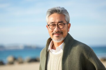 Fototapeta premium Portrait of a Japanese man in his 50s wearing a chic cardigan against a beach background