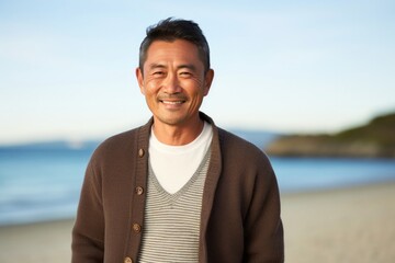 Portrait of a Japanese man in his 50s wearing a chic cardigan against a beach background