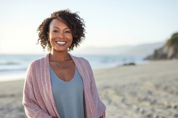Portrait of a confident Kenyan woman in her 40s wearing a chic cardigan against a beach background