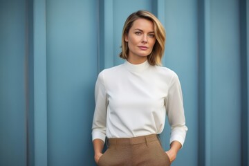 Portrait of a serious, Polish woman in her 30s wearing a smart pair of trousers against an abstract background