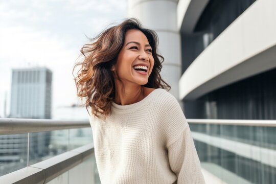 medium shot portrait of a happy Filipino woman in her 40s wearing a cozy sweater against a modern architectural background