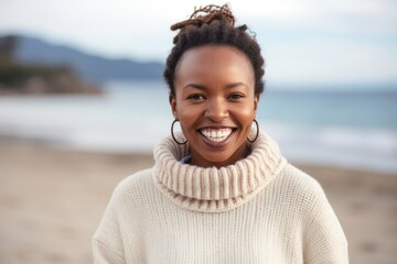medium shot portrait of a happy Kenyan woman in her 30s wearing a cozy sweater against a beach background