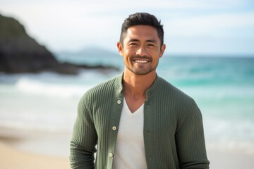 medium shot portrait of a happy Filipino man in his 30s wearing a chic cardigan against a beach background