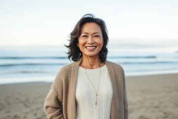 medium shot portrait of a happy Filipino woman in her 50s wearing a chic cardigan against a beach background
