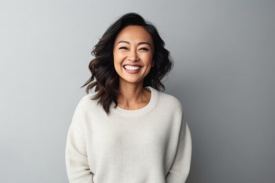 medium shot portrait of a happy Filipino woman in her 40s wearing a cozy sweater against a minimalist or empty room background