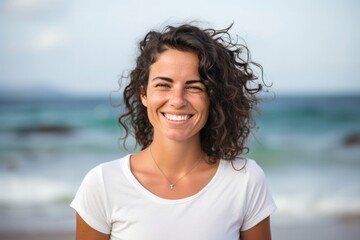 medium shot portrait of a happy Israeli woman in her 30s wearing a casual t-shirt against a beach background