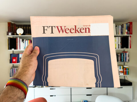 Paris, France - Sep 18, 2023: Man holds latest FT Weekend with front-page advertising, while Vitsoe shelves are visible in the background, merging news and modern design elements.