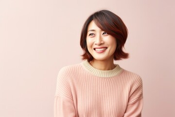 medium shot portrait of a happy Japanese woman in her 40s wearing a cozy sweater against a pastel or soft colors background