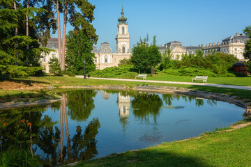 Festetics Palace with beautiful garden on sunny summer day, baroque architecture, Keszthely, Zala, Hungary. Outdoor travel background with green grass, trees, blue sky and pond with reflection