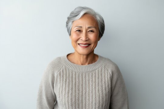 portrait of a happy Filipino woman in her 70s wearing a cozy sweater against a minimalist or empty room background