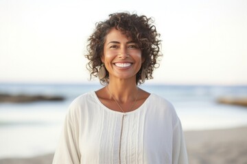medium shot portrait of a happy Mexican woman in her 50s wearing a simple tunic against a beach background